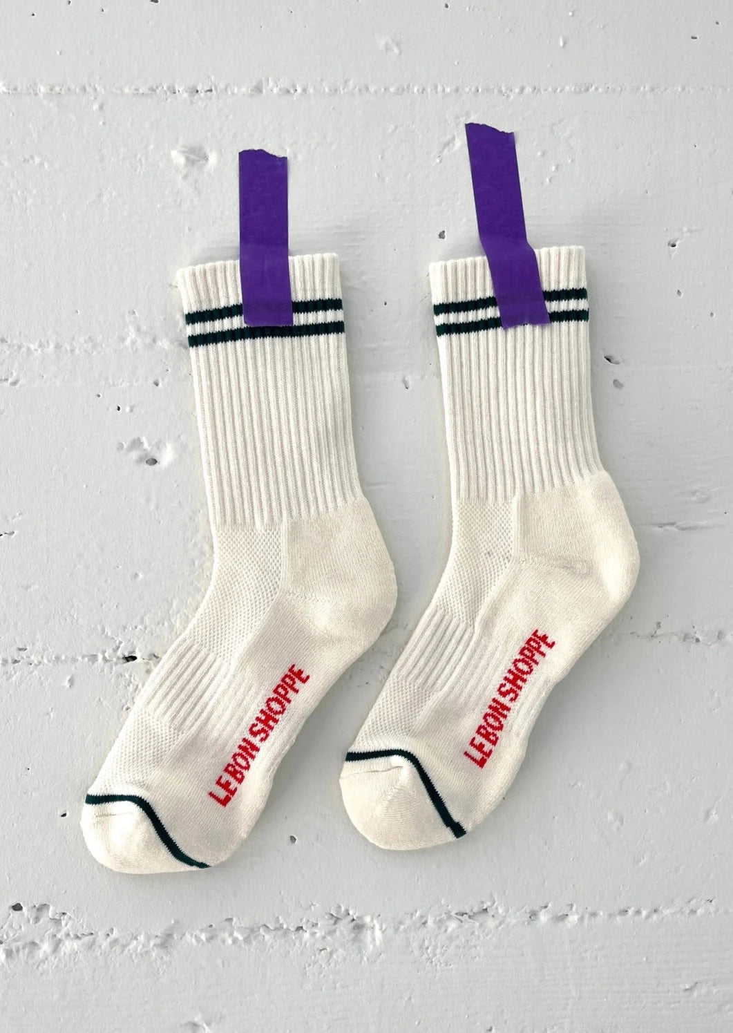 White socks with green stripes taped with purple tape to a white concrete wall.