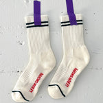White socks with green stripes taped with purple tape to a white concrete wall.