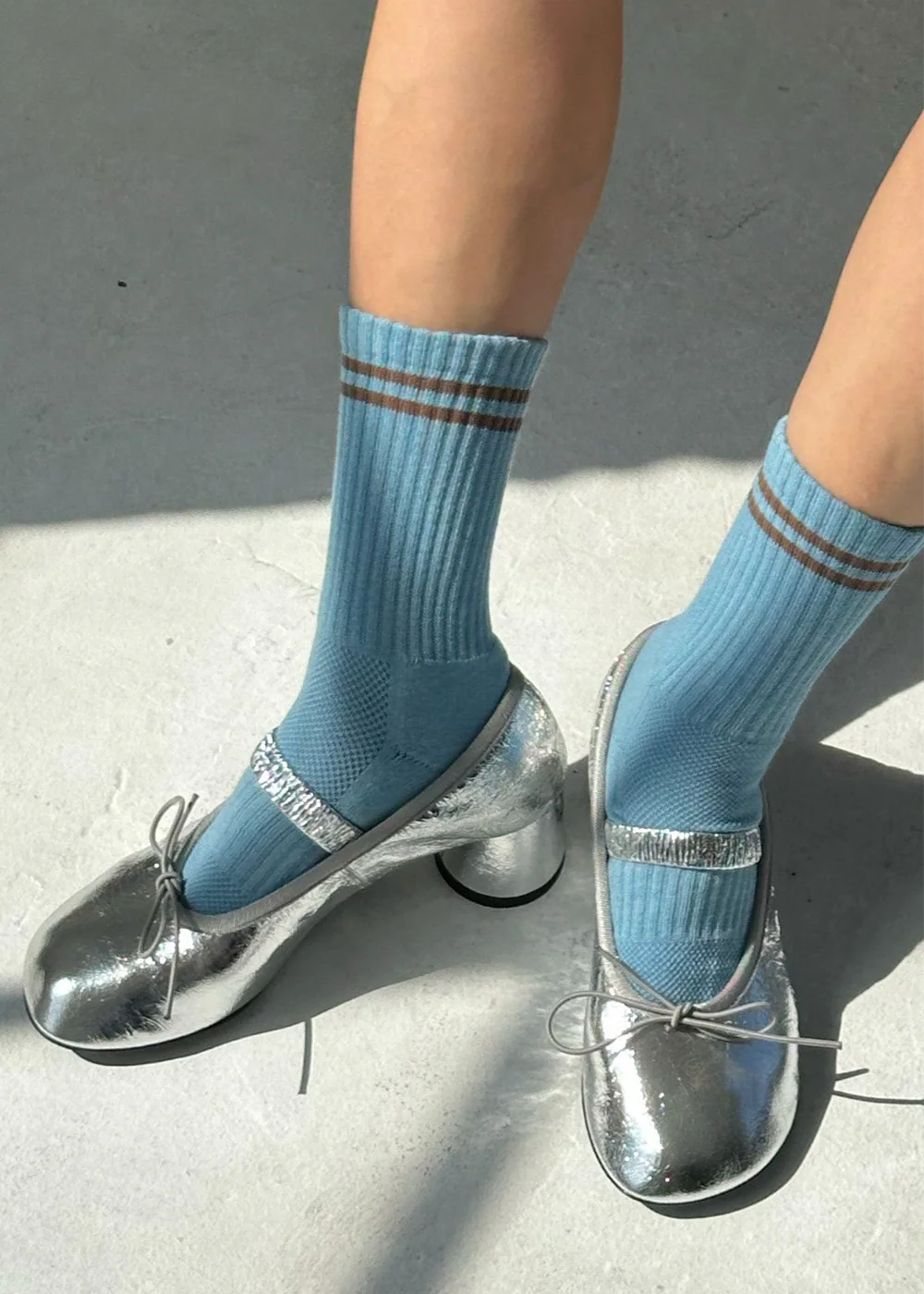 Blue socks with brown stripes worn with silver high-heeled shoes on a concrete surface.