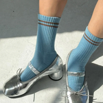 Blue socks with brown stripes worn with silver high-heeled shoes on a concrete surface.