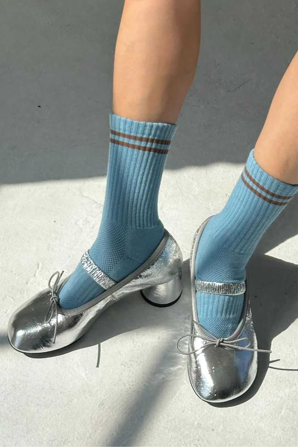 Blue socks with brown stripes worn with silver high-heeled shoes on a concrete surface.