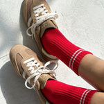 Beige sneakers with white laces worn with red socks on a light gray background