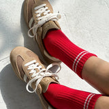 Beige sneakers with white laces worn with red socks on a light gray background