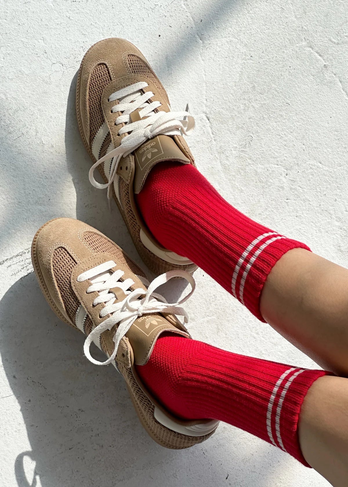 Beige sneakers with white laces worn with red socks on a light gray background