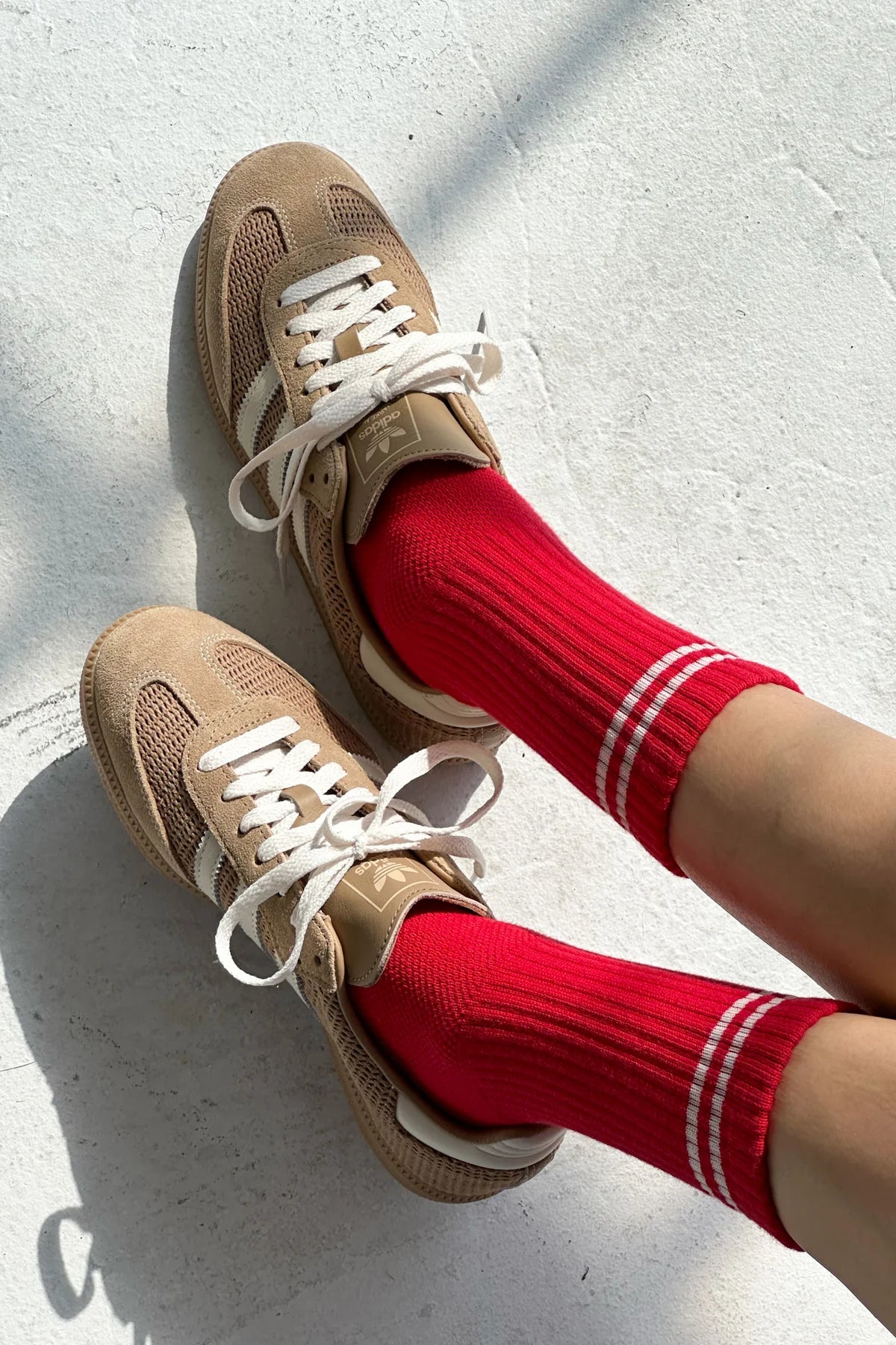 Beige sneakers with white laces worn with red socks on a light gray background