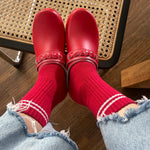 Red shoes and socks with light blue jeans on a wooden floor.