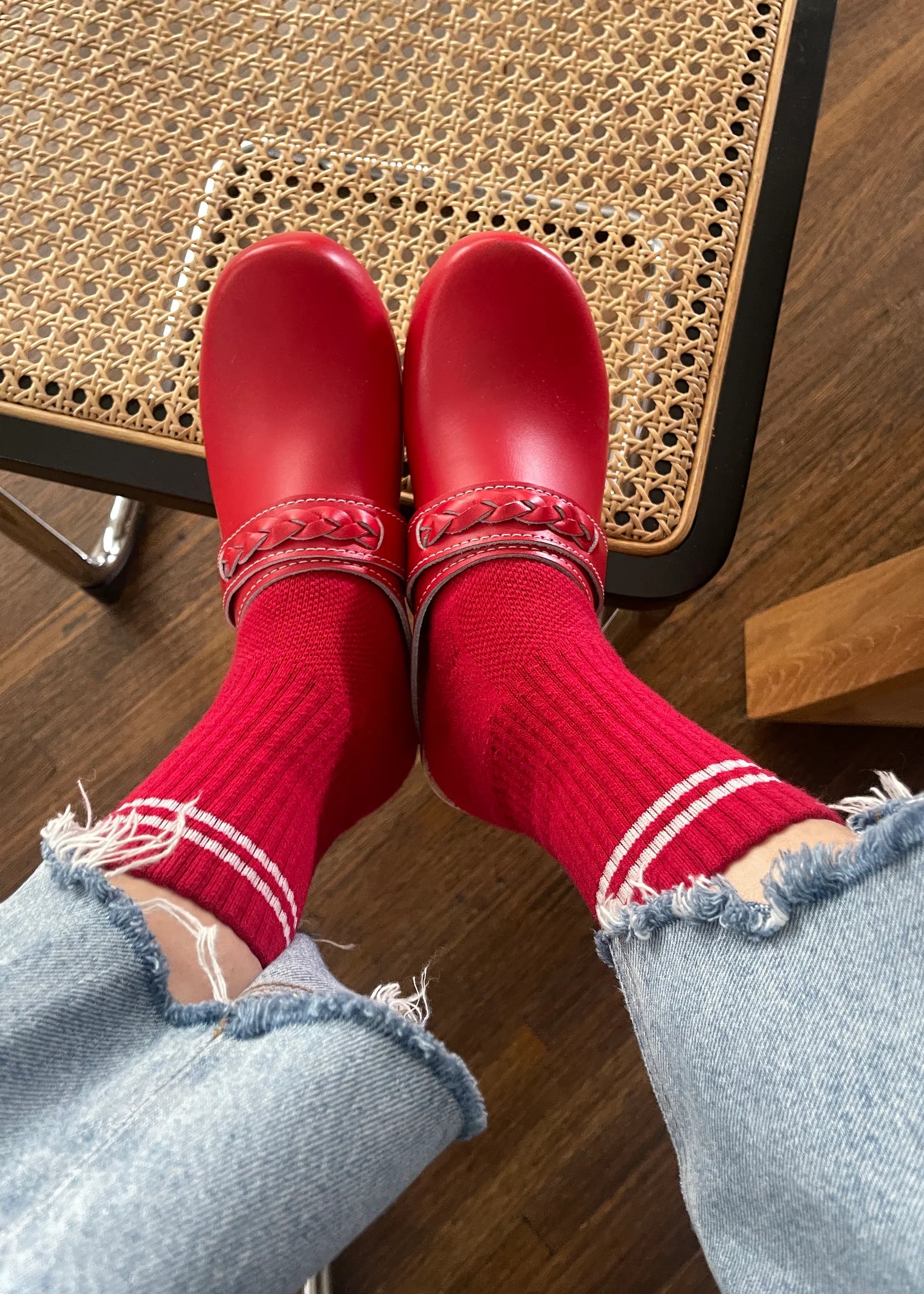 Red shoes and socks with light blue jeans on a wooden floor.