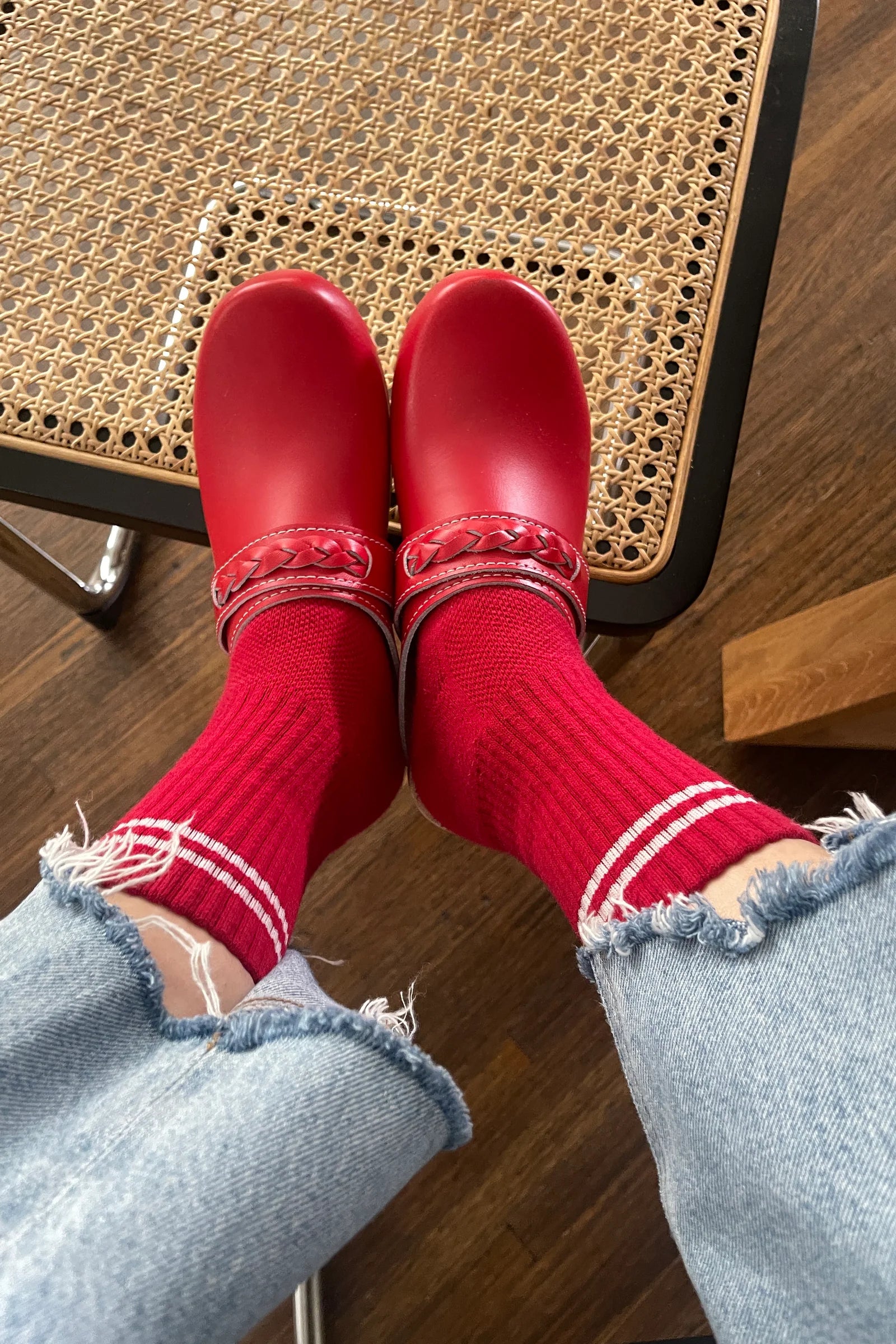 Red shoes and socks with light blue jeans on a wooden floor.