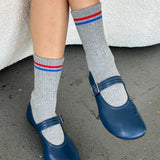 Person wearing grey socks with red and blue striped and blue mary jane shoes.