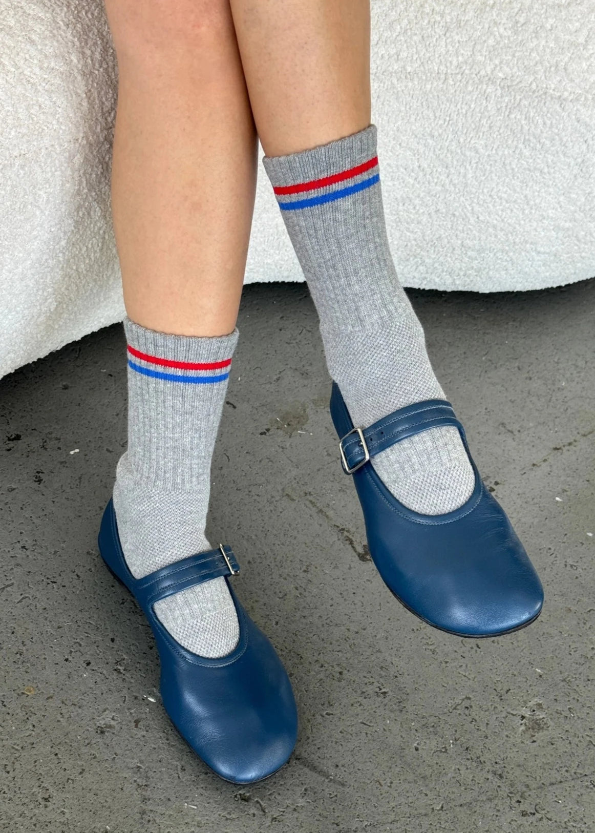 Person wearing grey socks with red and blue striped and blue mary jane shoes.