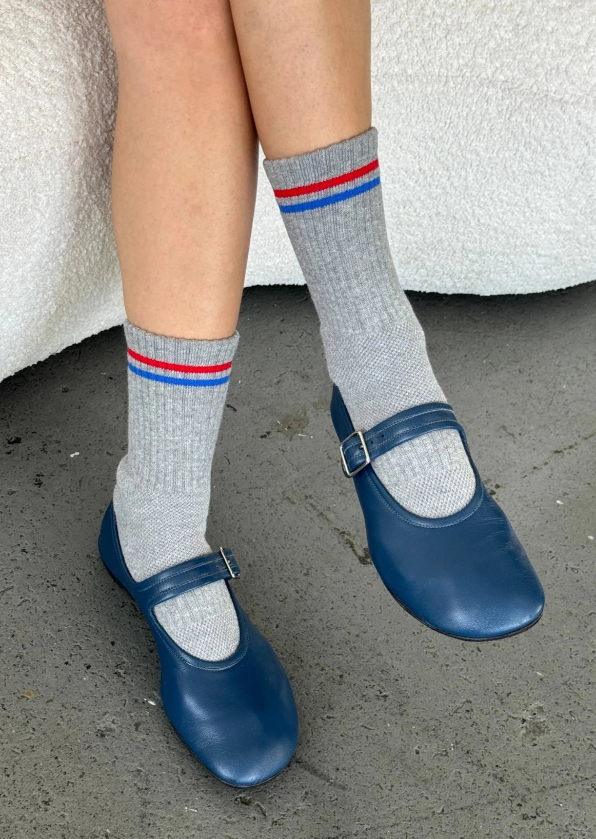 Person wearing grey socks with red and blue striped and blue mary jane shoes.