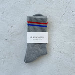 Grey socks with red and blue stripes and Le Bon Shoppe branding on a white background.