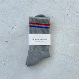 Grey socks with red and blue stripes and Le Bon Shoppe branding on a white background.