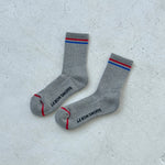 Grey socks with red and blue stripes and Le Bon Shoppe branding on a white background.