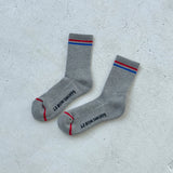 Grey socks with red and blue stripes and Le Bon Shoppe branding on a white background.