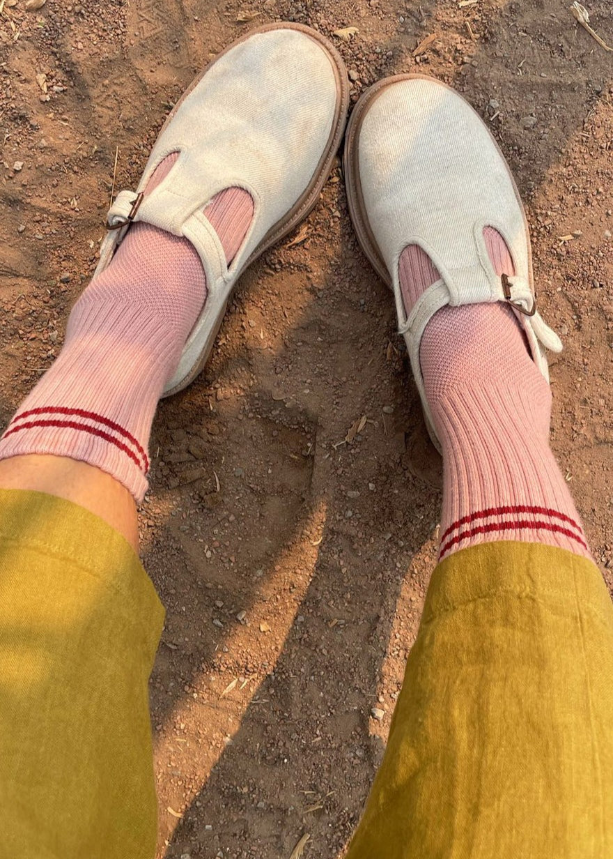 A pair of vintage pink socks with a contrasting double stripe, worn with light-colored shoes and yellow pants.