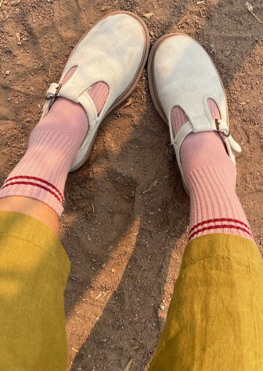 A pair of vintage pink socks with a contrasting double stripe, worn with light-colored shoes and yellow pants.