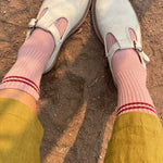 A pair of vintage pink socks with a contrasting double stripe, worn with light-colored shoes and yellow pants.