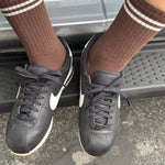 Person wearing black sneakers and brown socks with white stripes stepping onto a car.