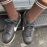 Person wearing black sneakers and brown socks with white stripes stepping onto a car.