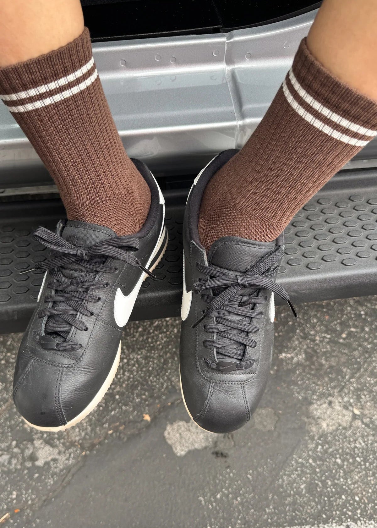 Person wearing black sneakers and brown socks with white stripes stepping onto a car.