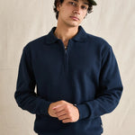 Man wearing a navy blue sweater and green cap against a beige background