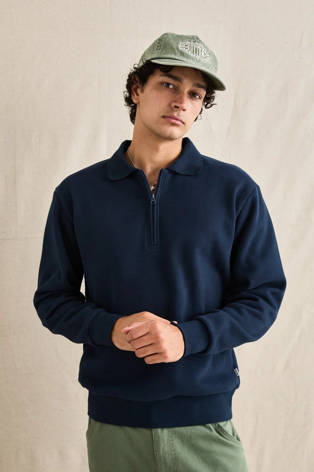 Man wearing a navy blue sweater and green cap against a beige background
