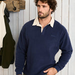 Man wearing a navy sweater with a white collar against a wooden wall.