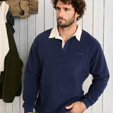 Man wearing a navy sweater with a white collar against a wooden wall.