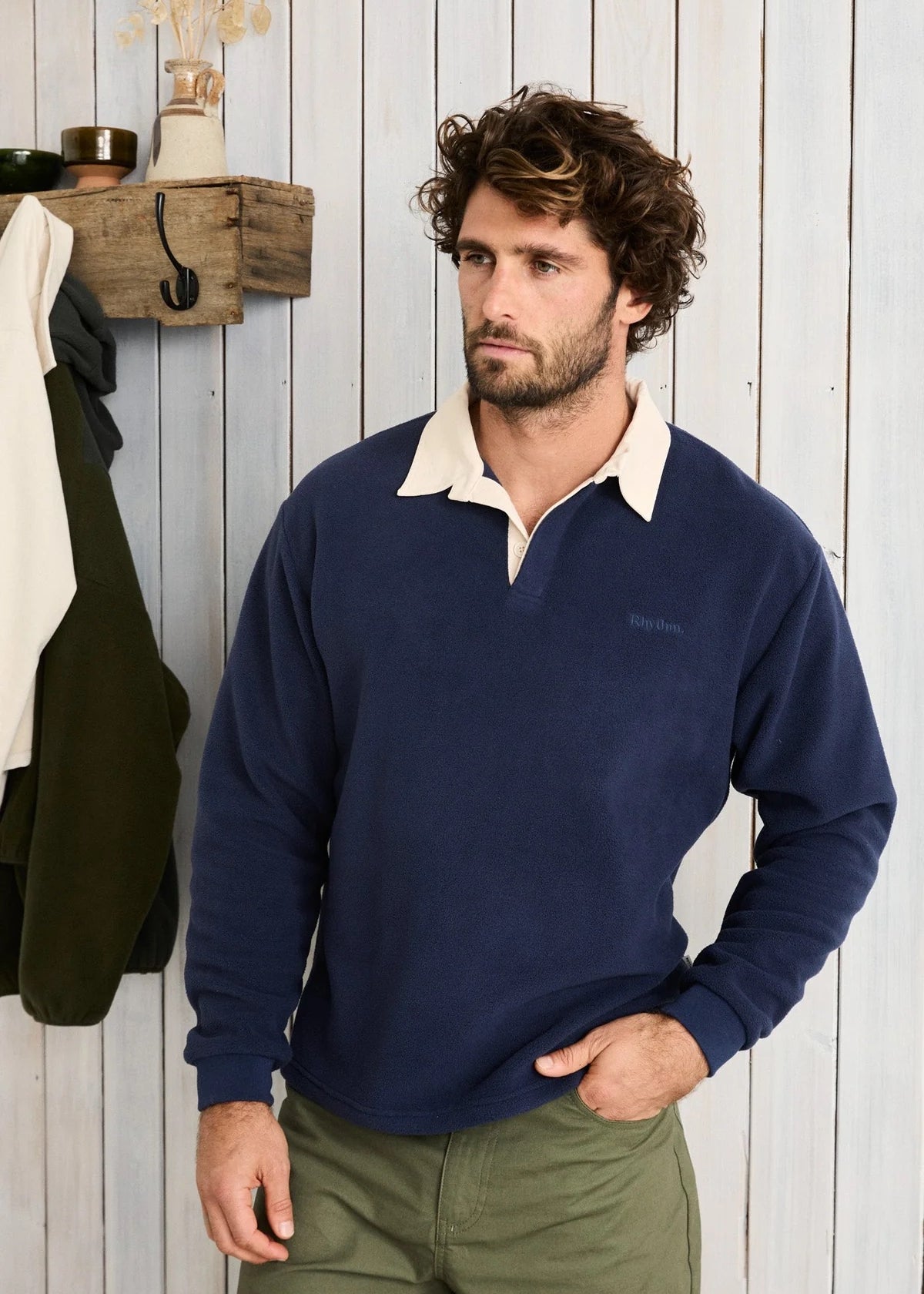 Man wearing a navy sweater with a white collar against a wooden wall.