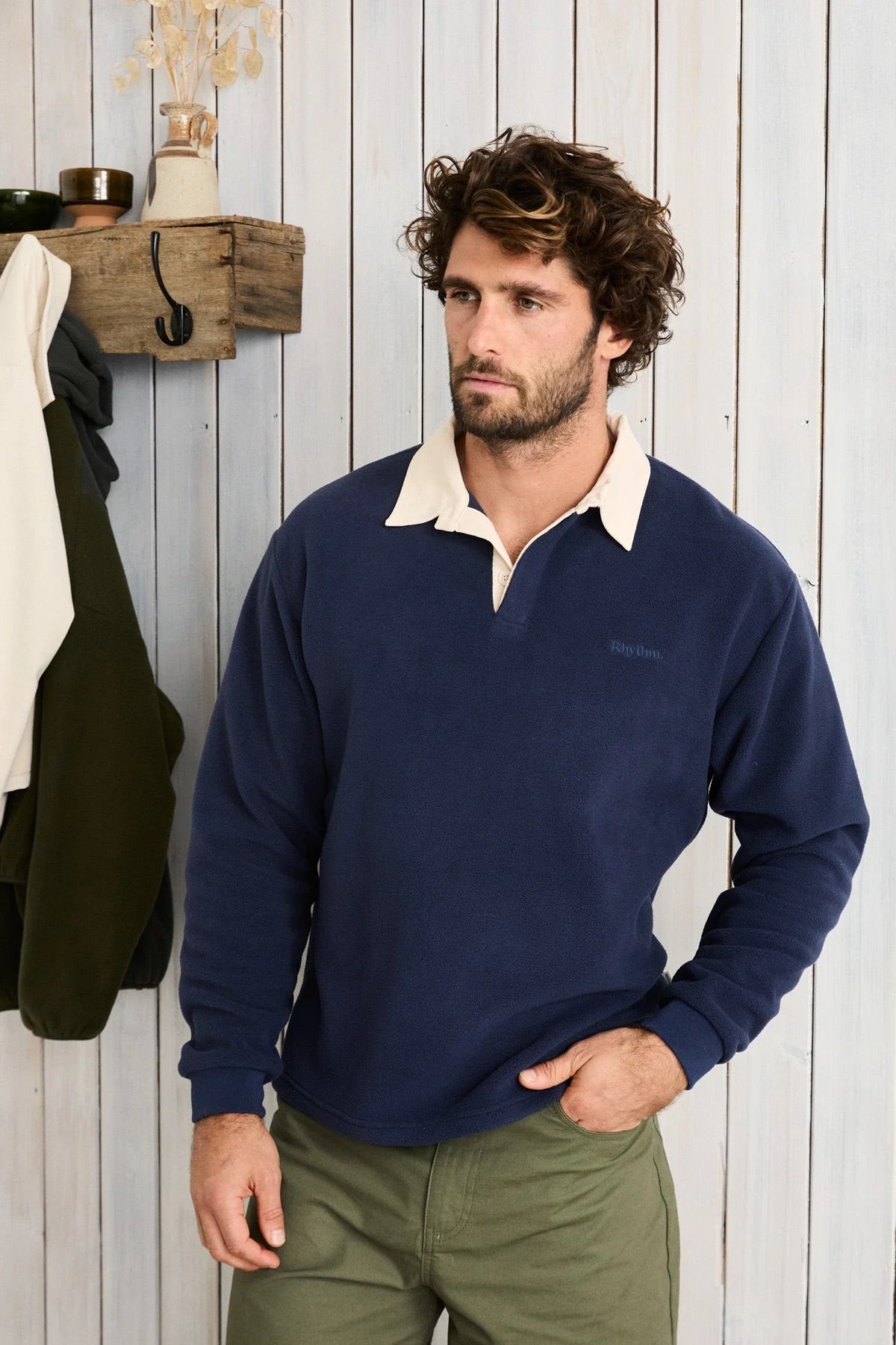 Man wearing a navy sweater with a white collar against a wooden wall.