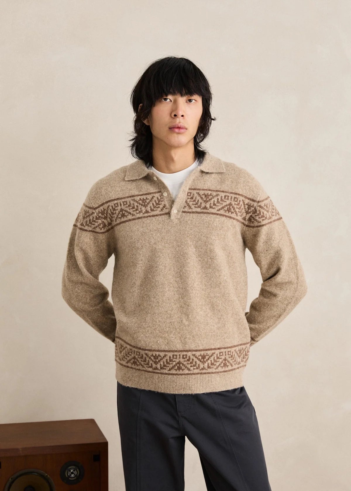 Man wearing a beige knitted sweater with patterned details against a plain background
