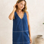 Woman wearing a blue denim dress against a white wall.