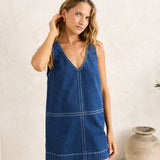 Woman wearing a blue denim dress against a white wall.