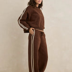 Woman wearing a brown tracksuit with white stripes on a beige background