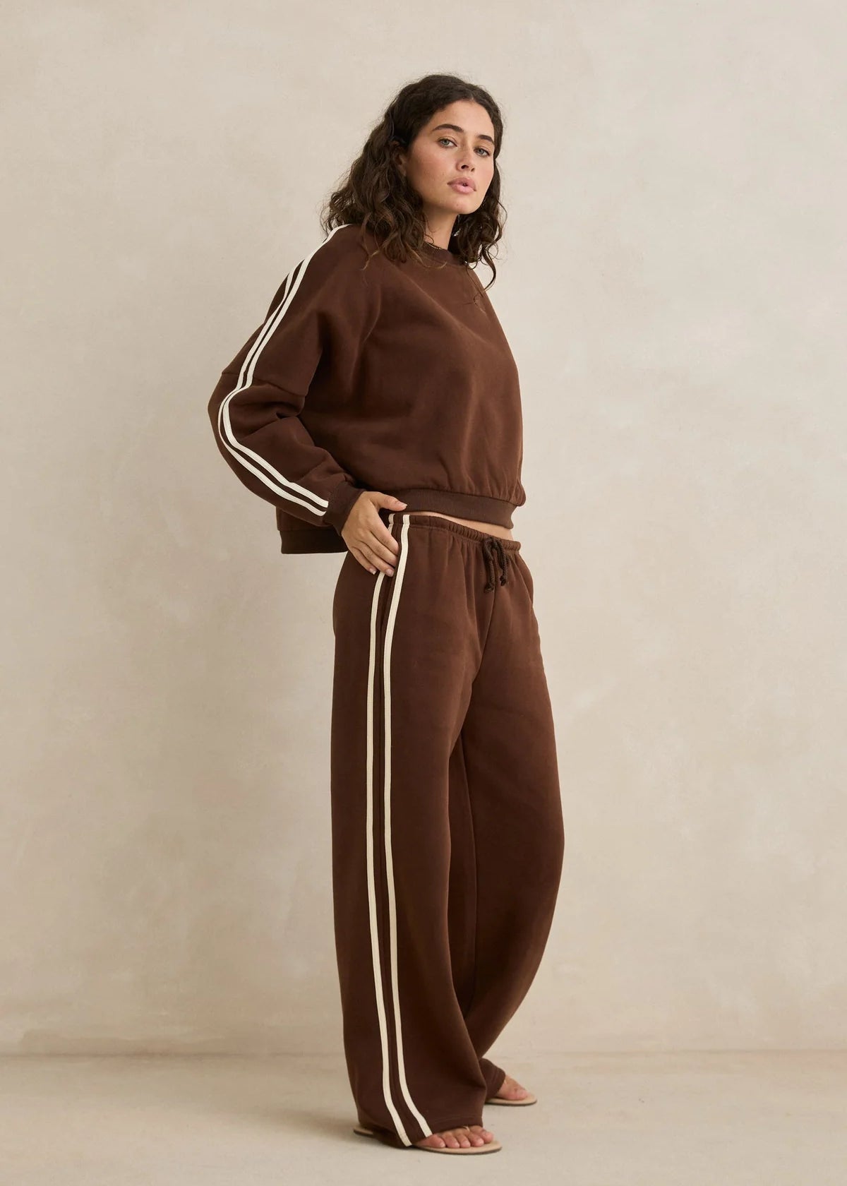 Woman wearing a brown tracksuit with white stripes on a beige background
