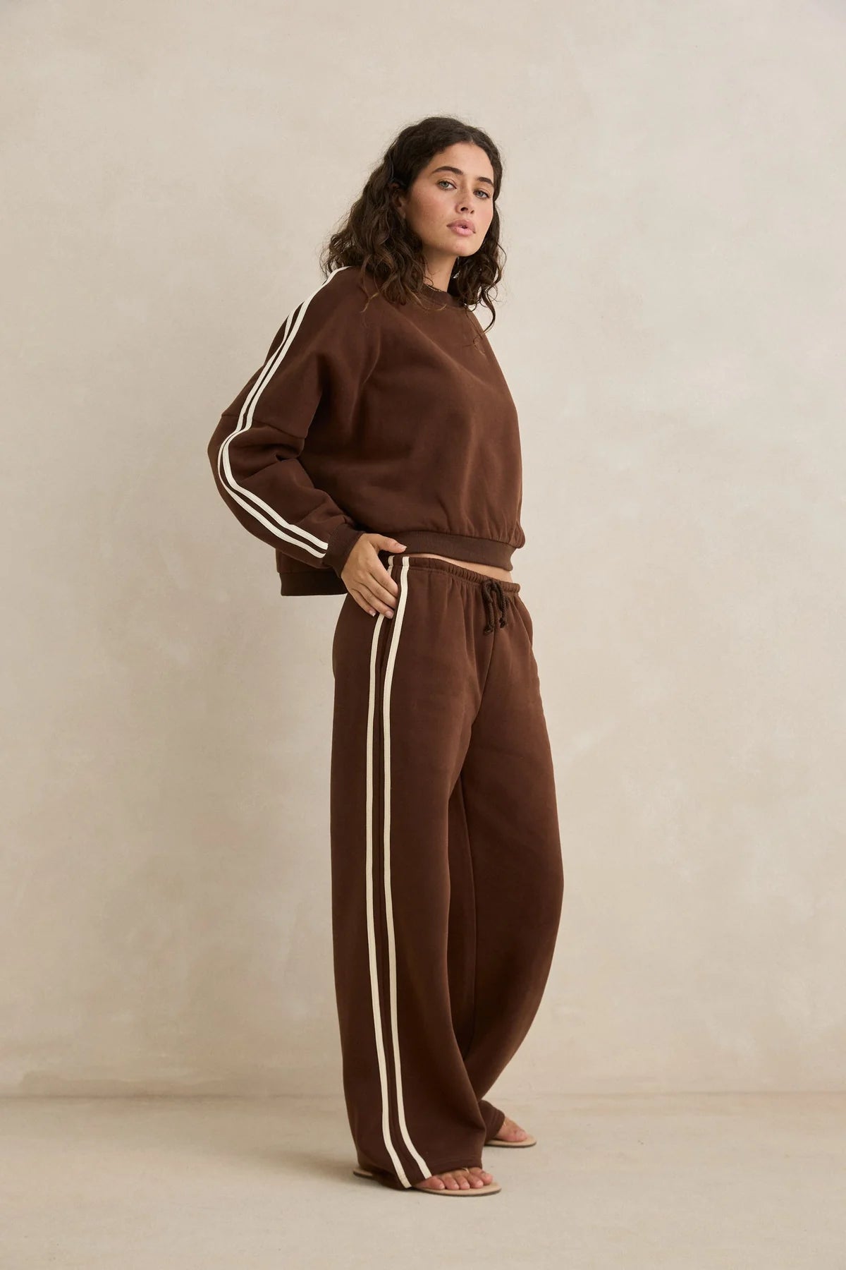 Woman wearing a brown tracksuit with white stripes on a beige background