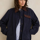 Woman wearing a navy jacket with brown accents against a beige background