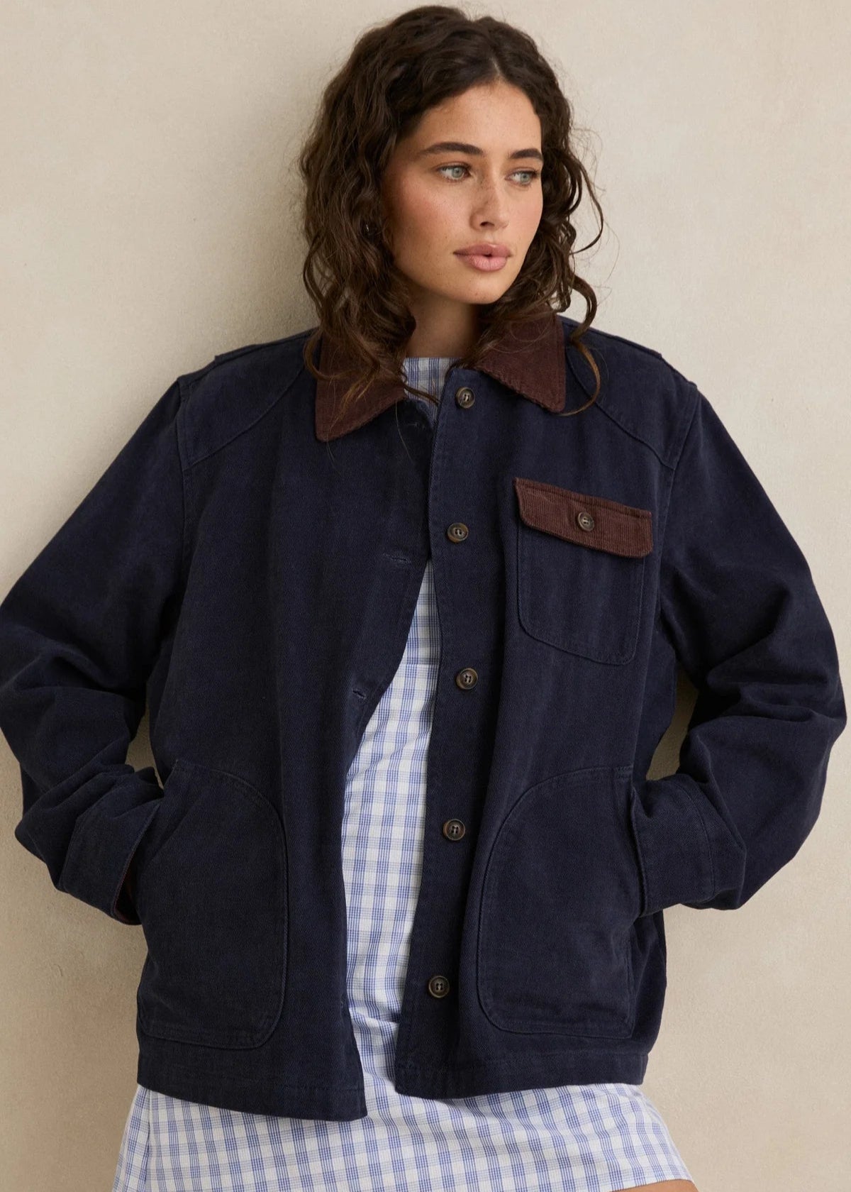 Woman wearing a navy jacket with brown accents against a beige background