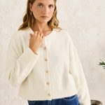 Woman wearing a cream cardigan and blue jeans against a white background