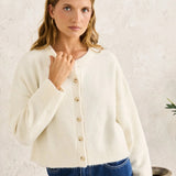 Woman wearing a cream cardigan and blue jeans against a white background