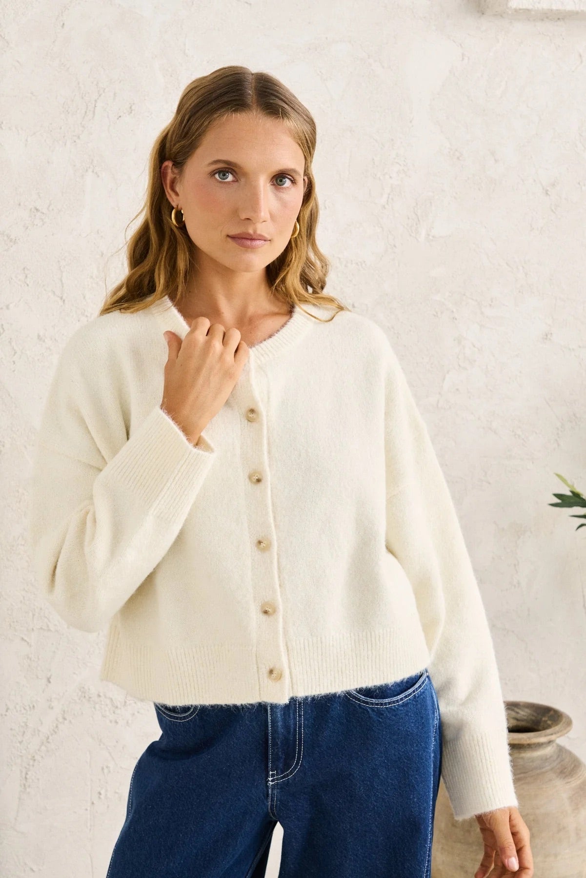 Woman wearing a cream cardigan and blue jeans against a white background