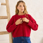Woman wearing a red sweater and blue jeans standing next to a wooden ladder indoors.