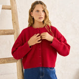 Woman wearing a red sweater and blue jeans standing next to a wooden ladder indoors.