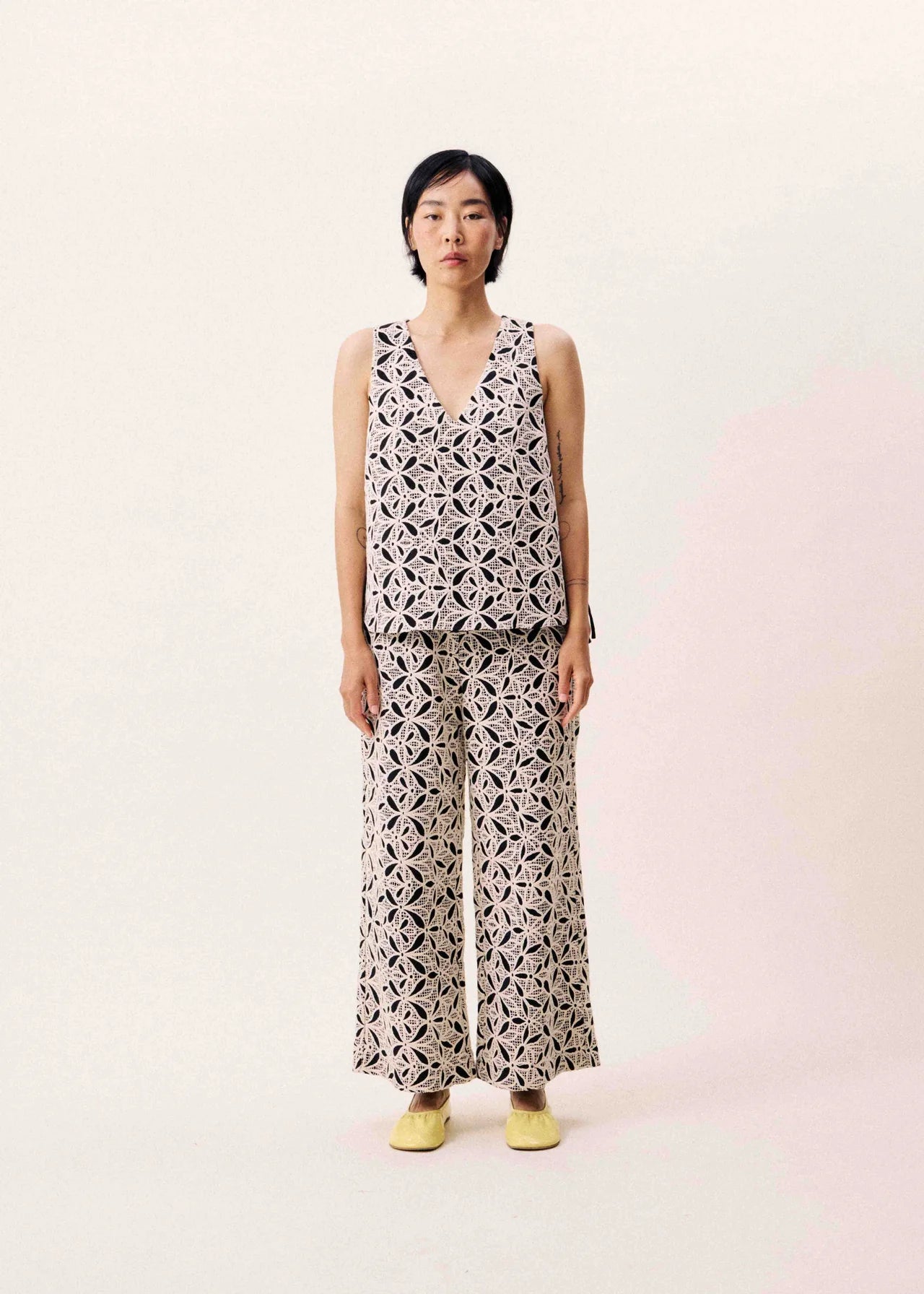Person wearing a sleeveless patterned top and wide-leg pants on a light pink background
