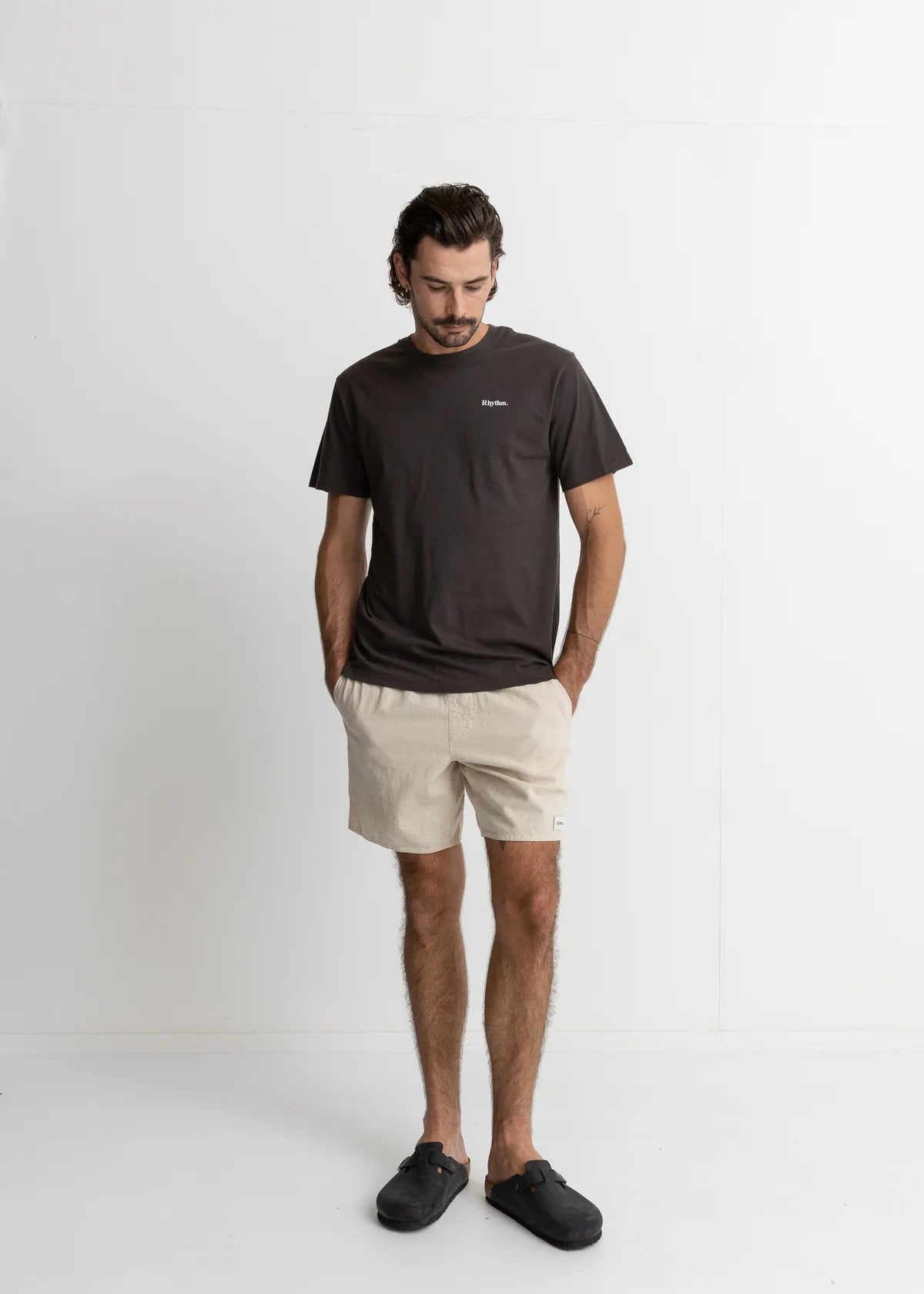Man wearing a dark t-shirt and beige shorts on a white background