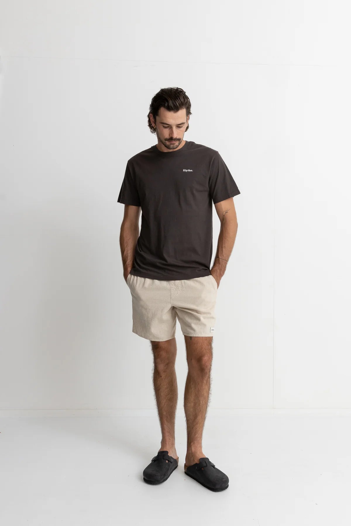 Man wearing a dark t-shirt and beige shorts on a white background
