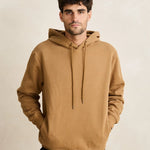 Man wearing a brown hoodie against a beige background