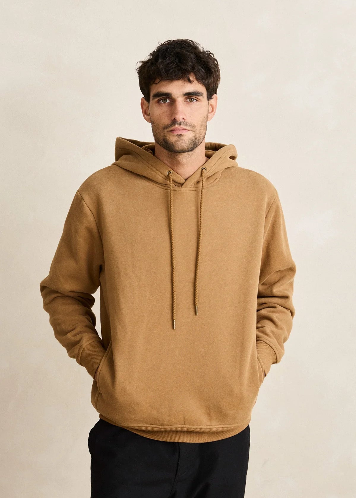 Man wearing a brown hoodie against a beige background