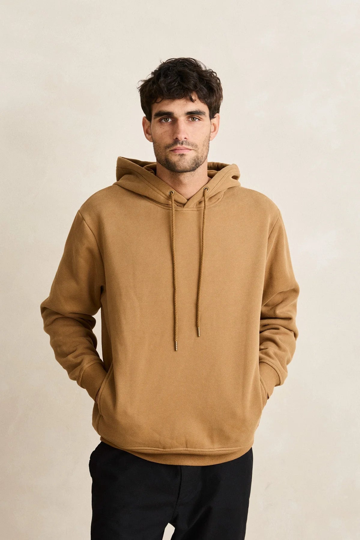 Man wearing a brown hoodie against a beige background